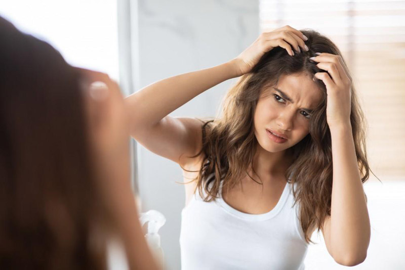 A woman gazes into a mirror, gently combing her hair with a focused expression.